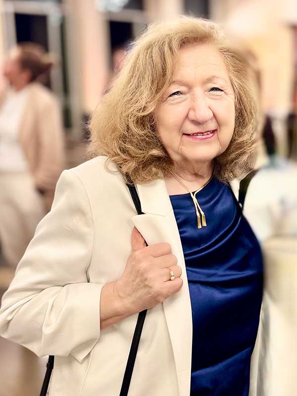 Jutta Shaikh Frau mit hellem Blazer und blauer Bluse vor unscharfem Hintergrund